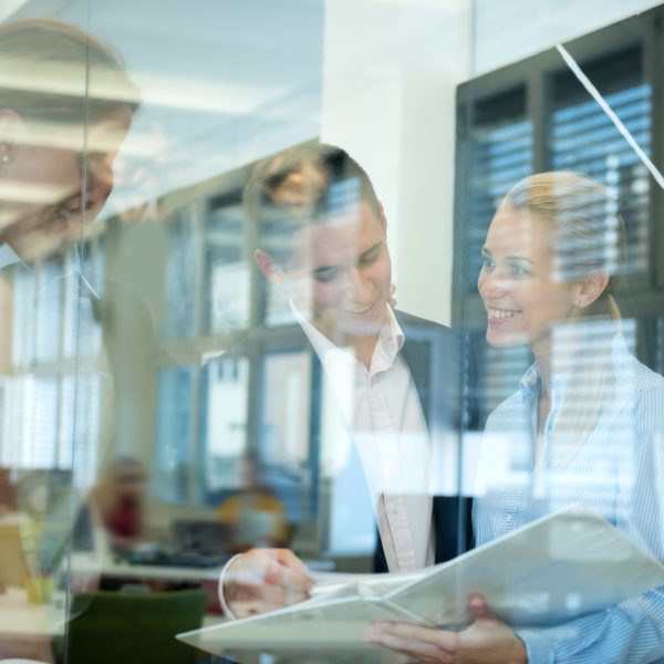 Smiling business team behind glass wall in office looking at folder